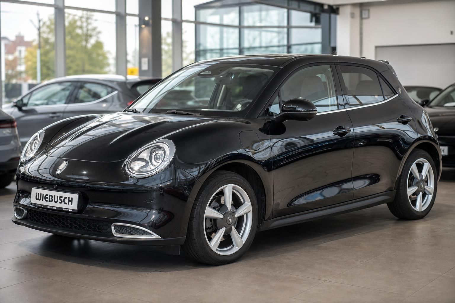 Schwarzer Kleinwagen in modernem Autohaus-Showroom mit großen Fenstern und weiteren Fahrzeugen im Hintergrund