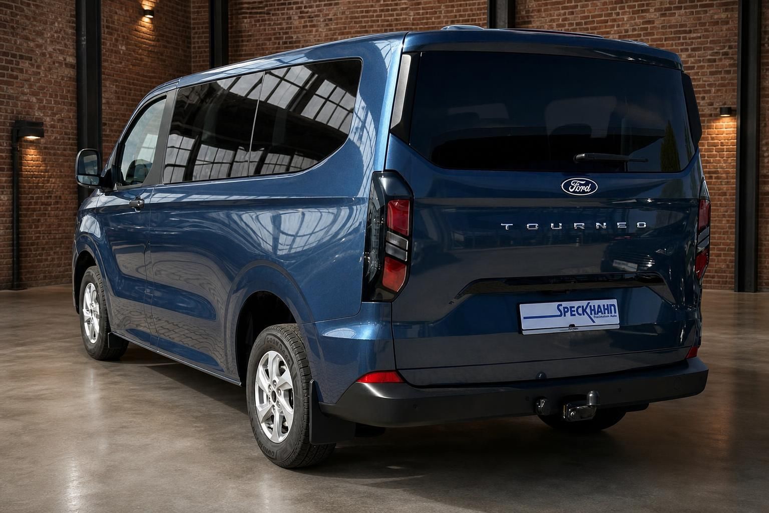 Ford Tourneo Custom blau, Heckansicht schraeg in Halle mit Ziegelwand