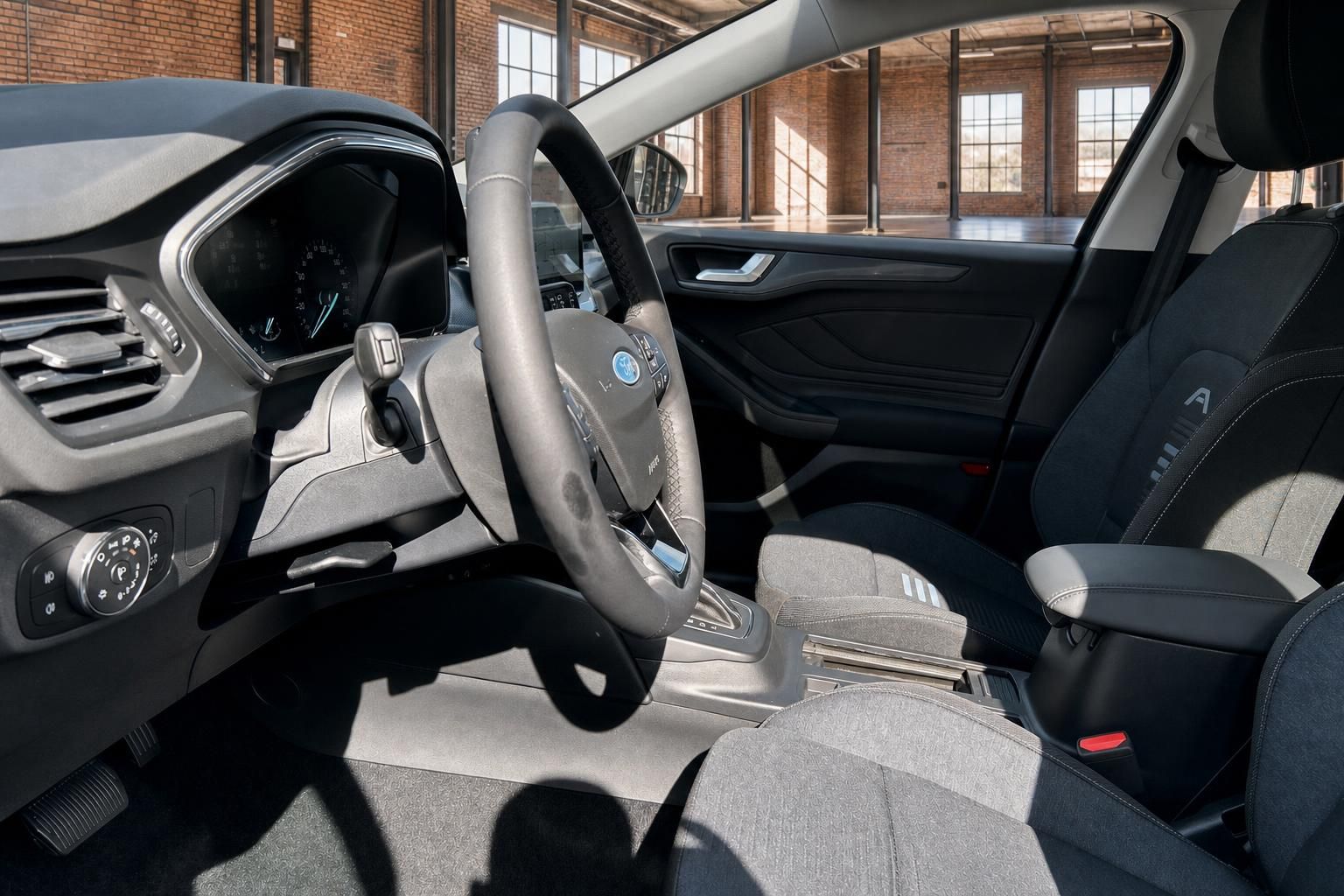 Ford Innenraum Fahrerseite mit Lenkrad, Armaturenbrett und Vordersitzen in grauem Stoff