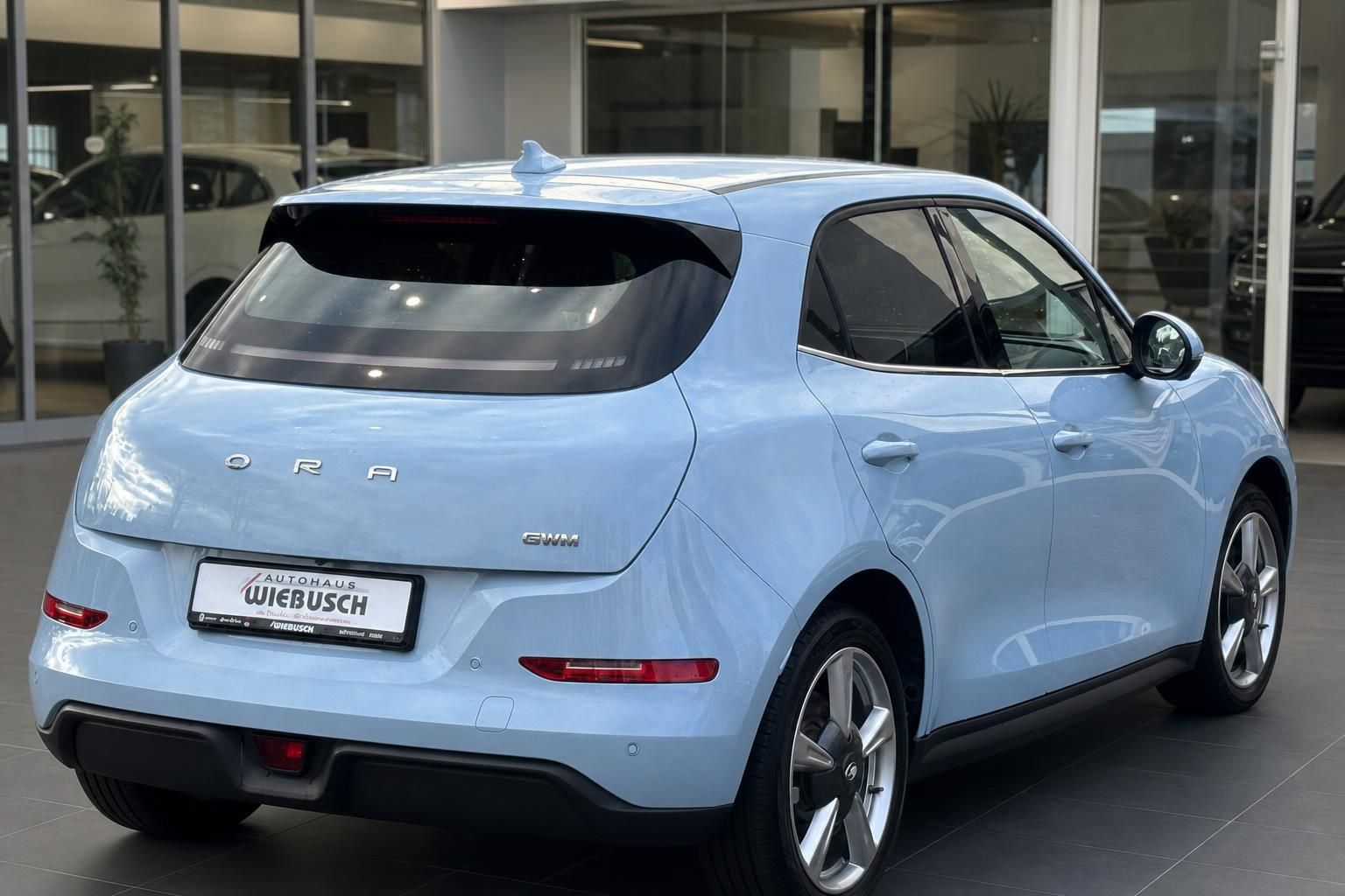 Hellblaues ORA Elektrofahrzeug - Seitliche Heckansicht im Autohaus-Showroom