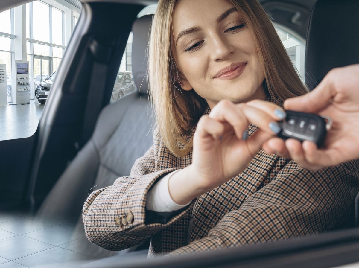 Frau erhält Autoschlüssel im Autohaus – Fahrzeugübergabe im Innenraum