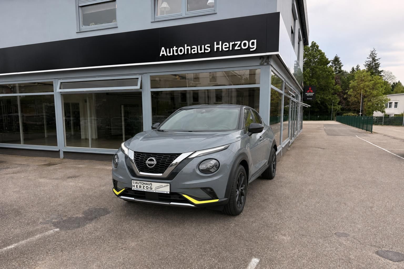Nissan Juke grau Frontansicht mit gelbem Unterfahrschutz vor Autohaus