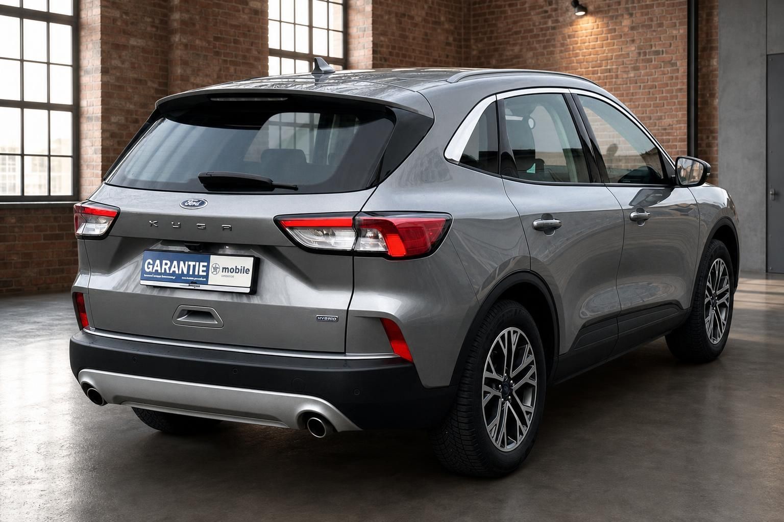 Ford Kuga Hybrid grau Heckansicht schraeg vor Backsteinwand