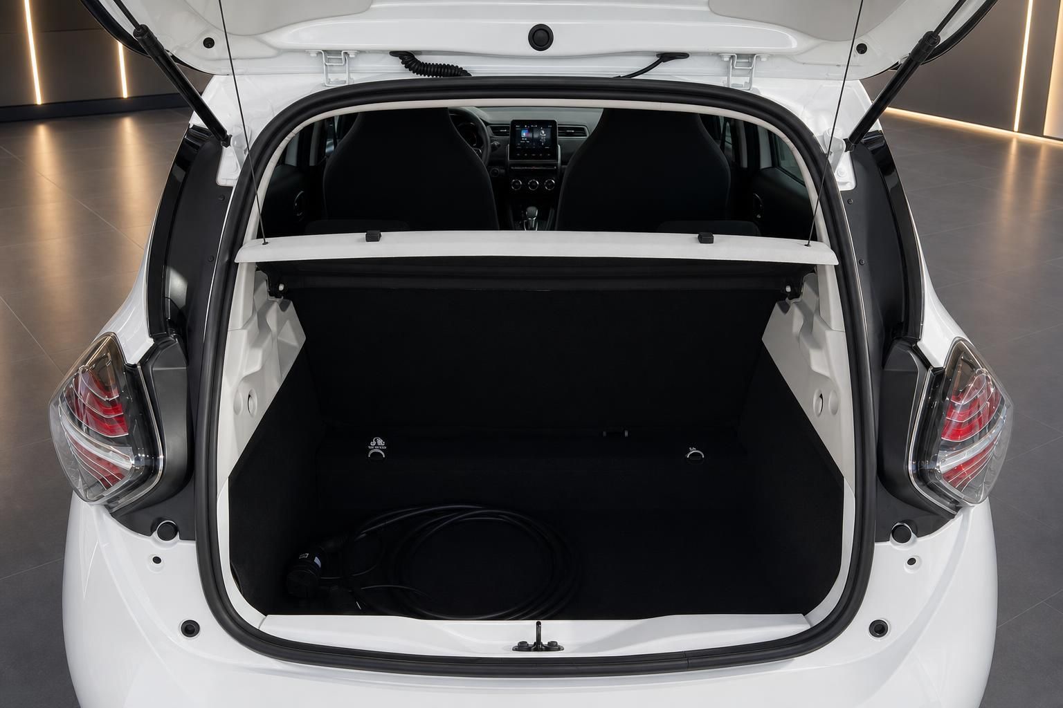 Geöffneter Kofferraum eines weißen Elektrofahrzeugs mit Ladekabel und schwarzer Kofferraum-Abdeckung