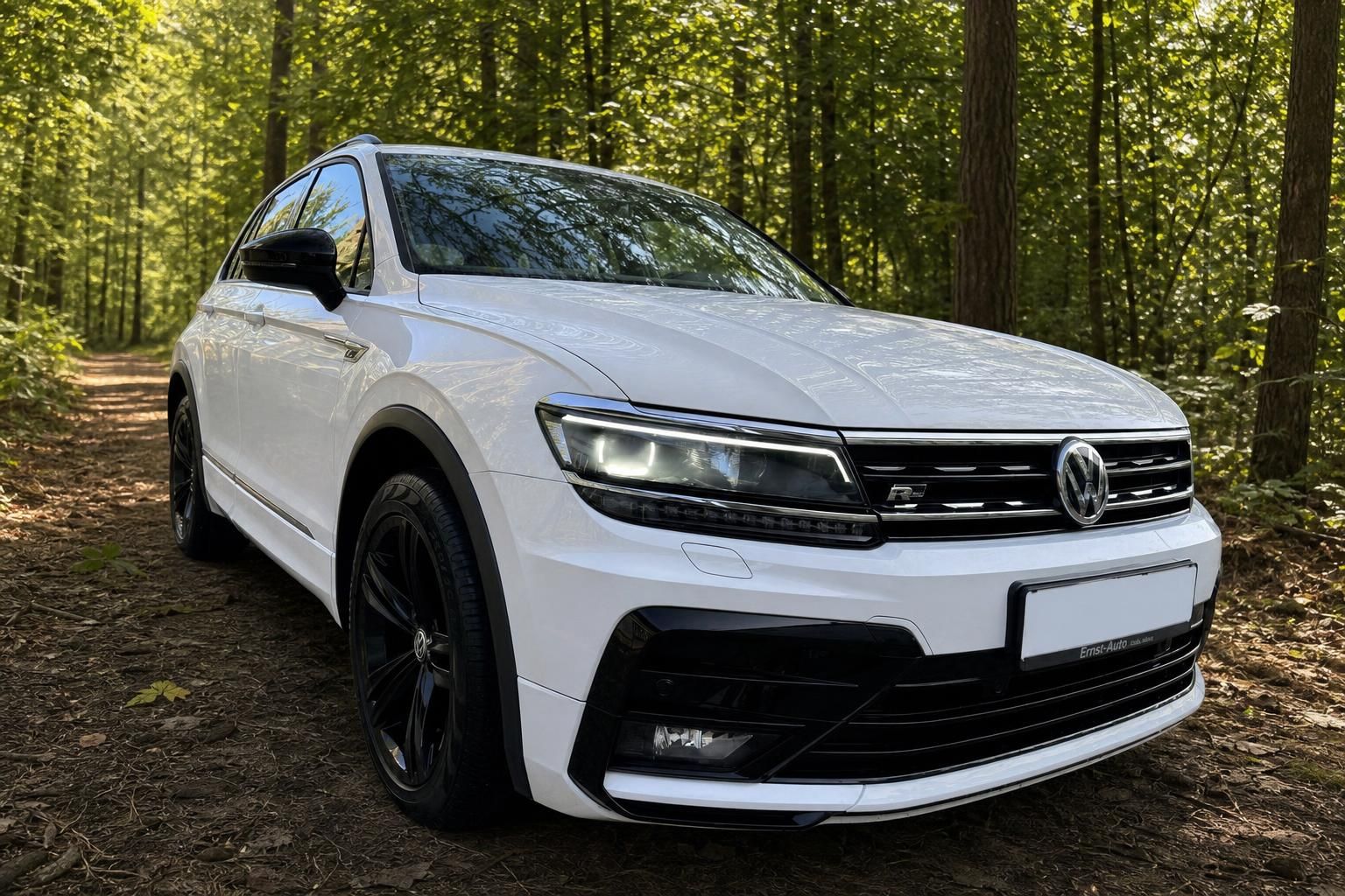 Weißer Volkswagen Tiguan SUV Frontansicht mit schwarzen Felgen im Waldweg - Gebrauchtwagen kaufen