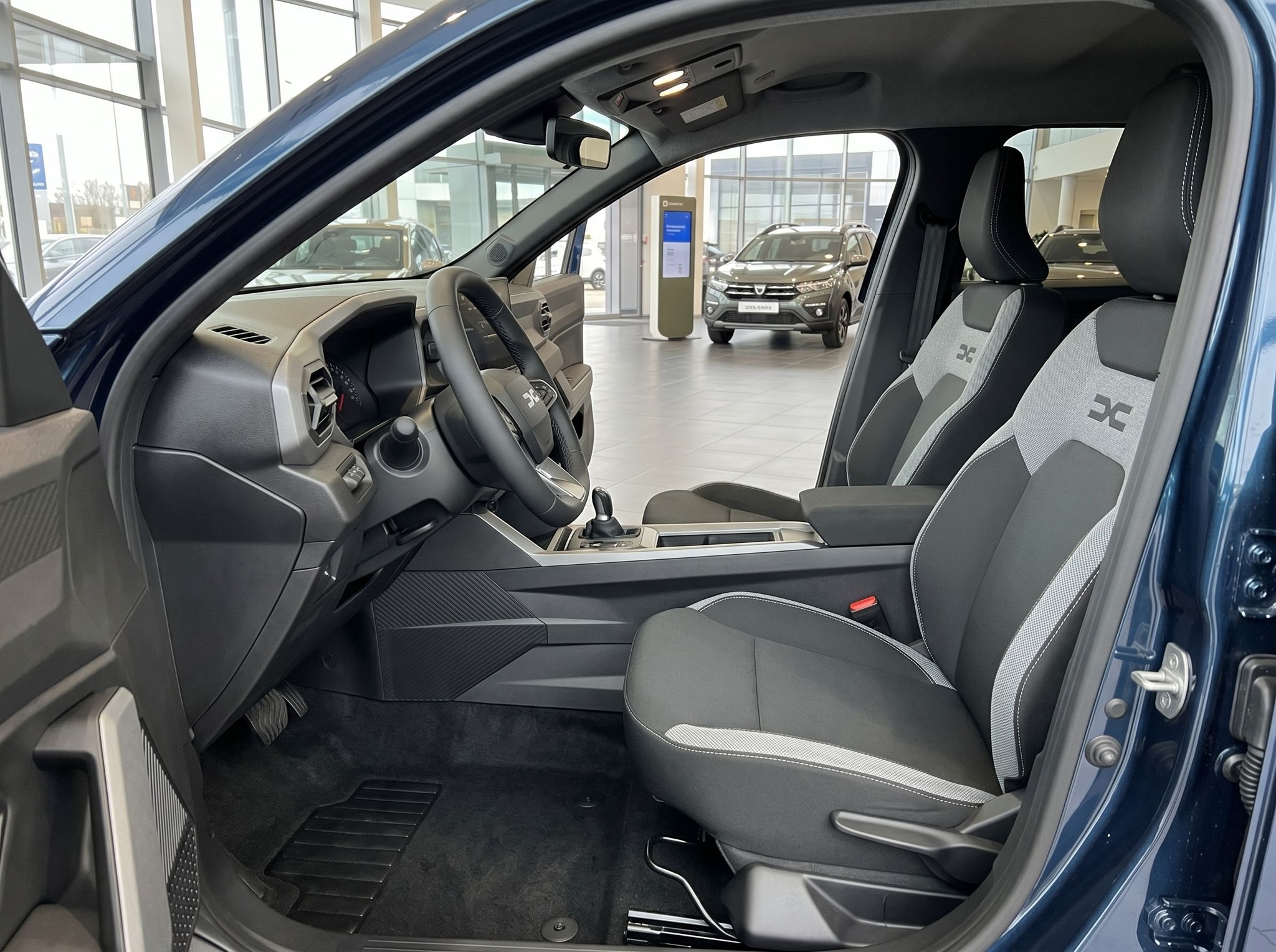 Fahrzeuginnenraum mit Fahrer- und Beifahrersitz, Lenkrad und Blick in den Autohaus-Showroom