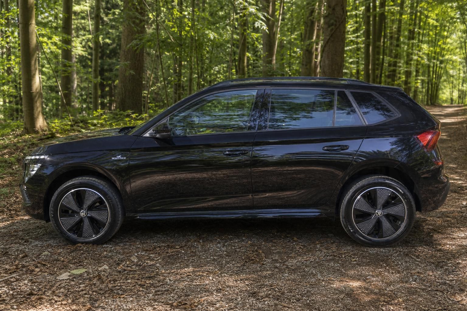 Schwarzer Skoda Kamiq SUV rechte Fahrzeugseite mit Alufelgen im Waldambiente