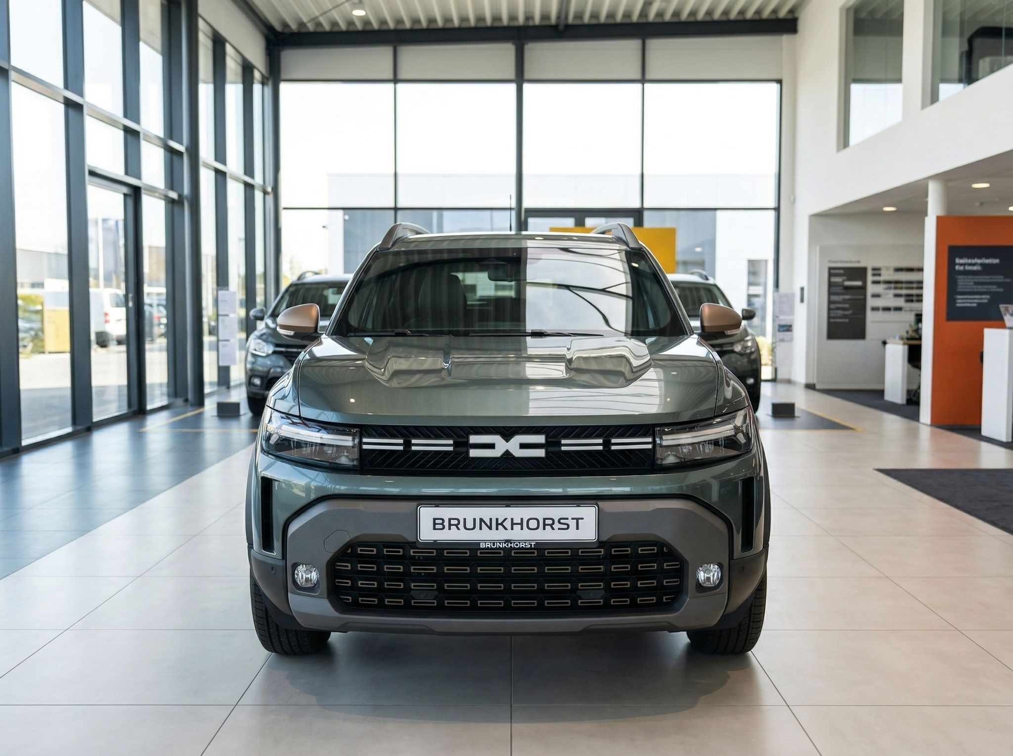 Dacia SUV Frontansicht in graugrün mit Brunkhorst Kennzeichen im modernen Autohaus-Showroom