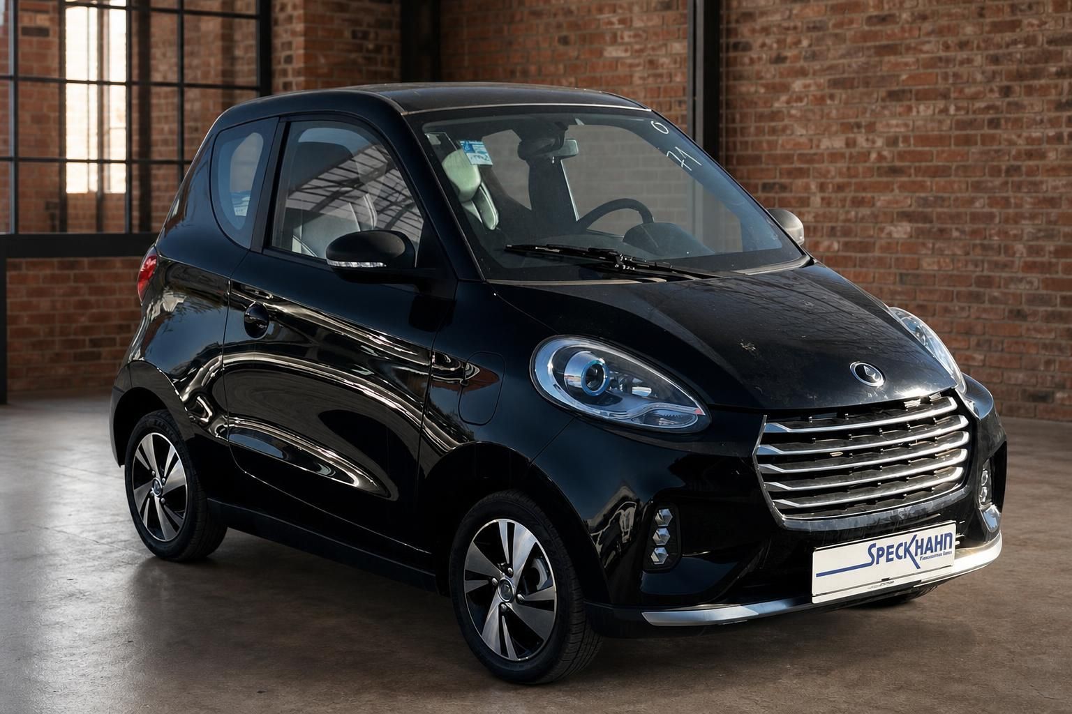 Schwarzer Kleinwagen in Frontansicht vor Backsteinwand im Autohaus