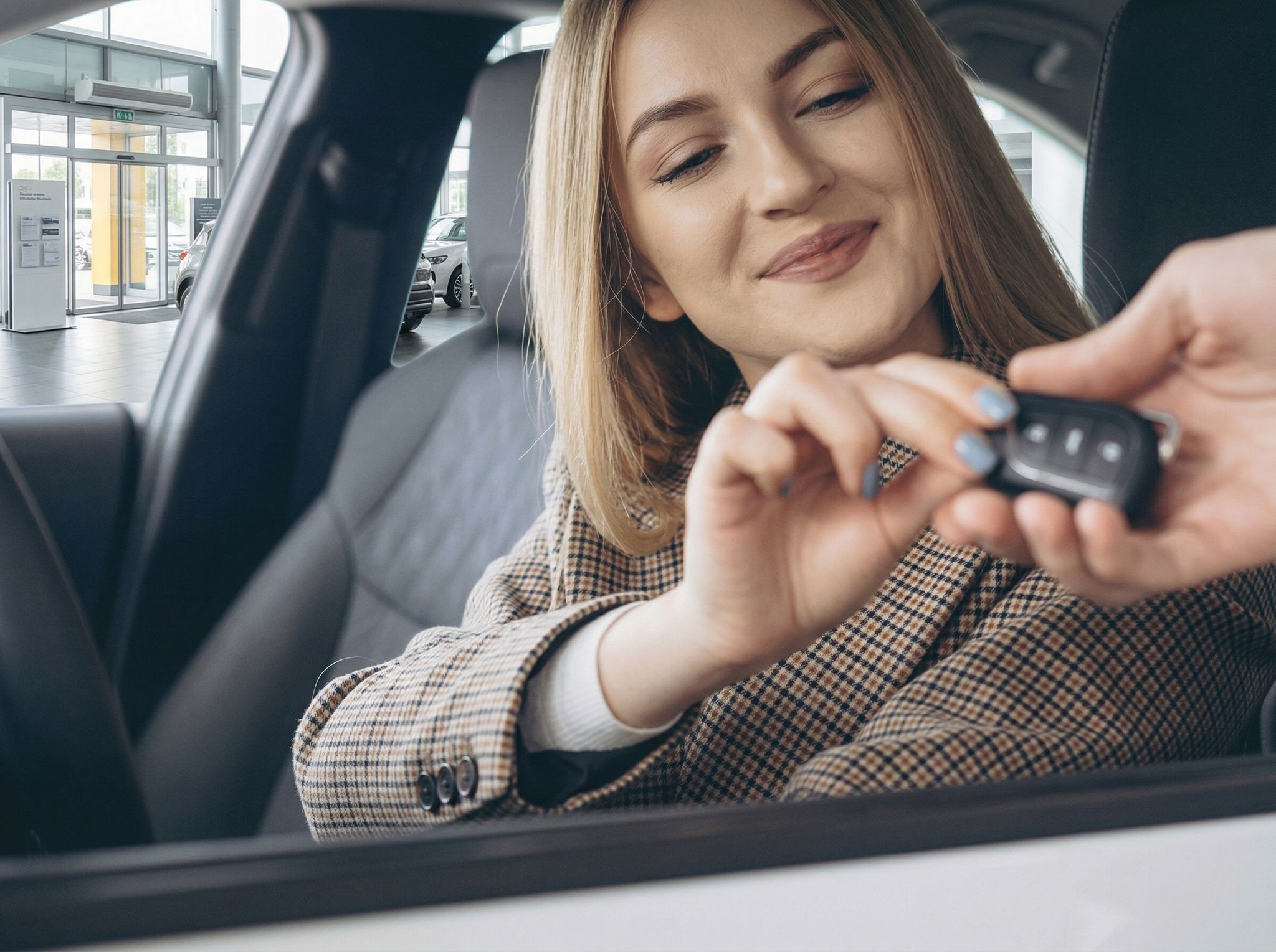 Frau mit Autoschlüssel im Fahrzeug-Innenraum - Fahrzeugübergabe beim Autohändler