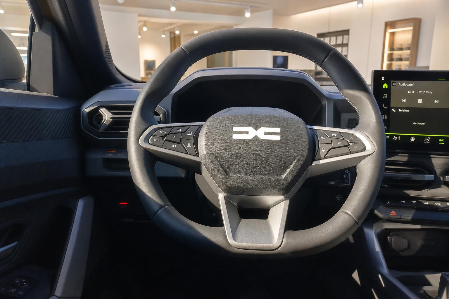 Lenkrad mit Bedienelementen und Markenlogo im Cockpit