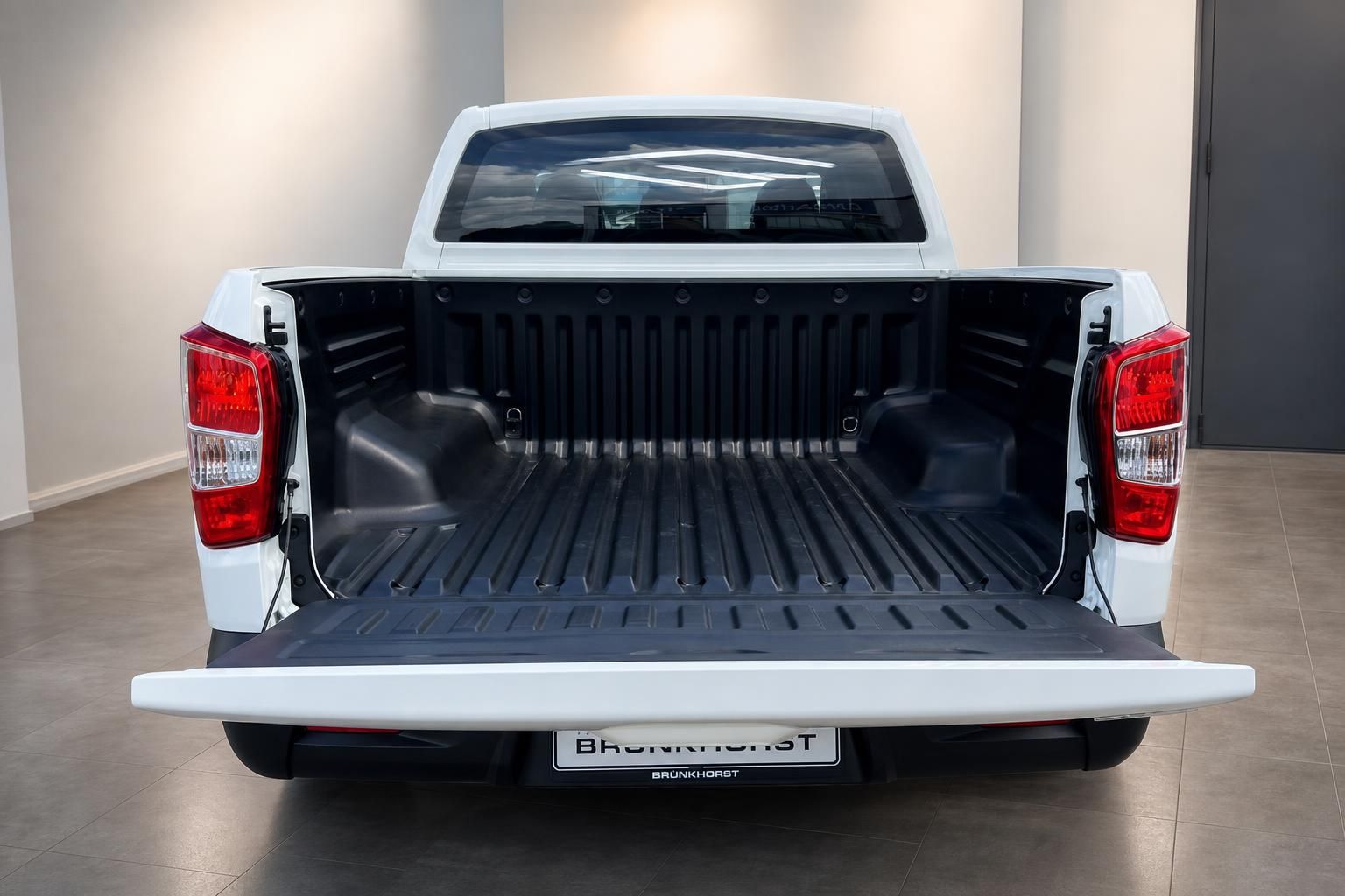Offene Ladefläche eines weißen Pickup-Trucks mit schwarzer Kunststoffauskleidung von hinten