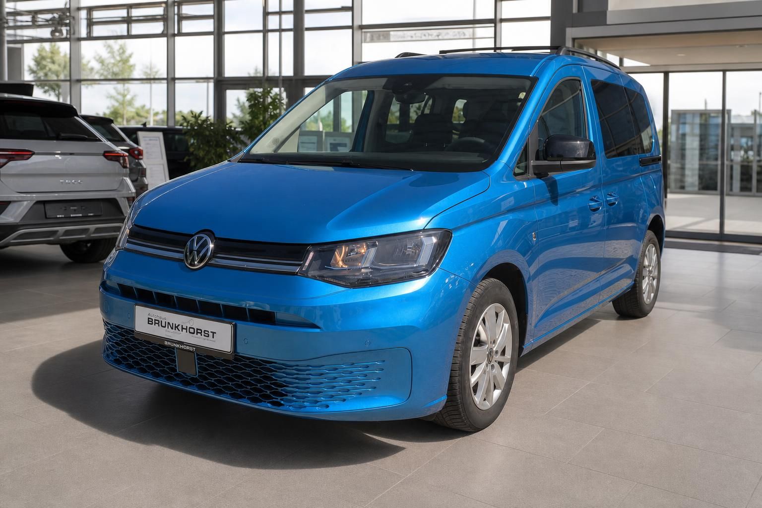 Volkswagen Caddy blau Seitenansicht im modernen Autohaus Showroom mit BRUNKHORST Kennzeichenhalter