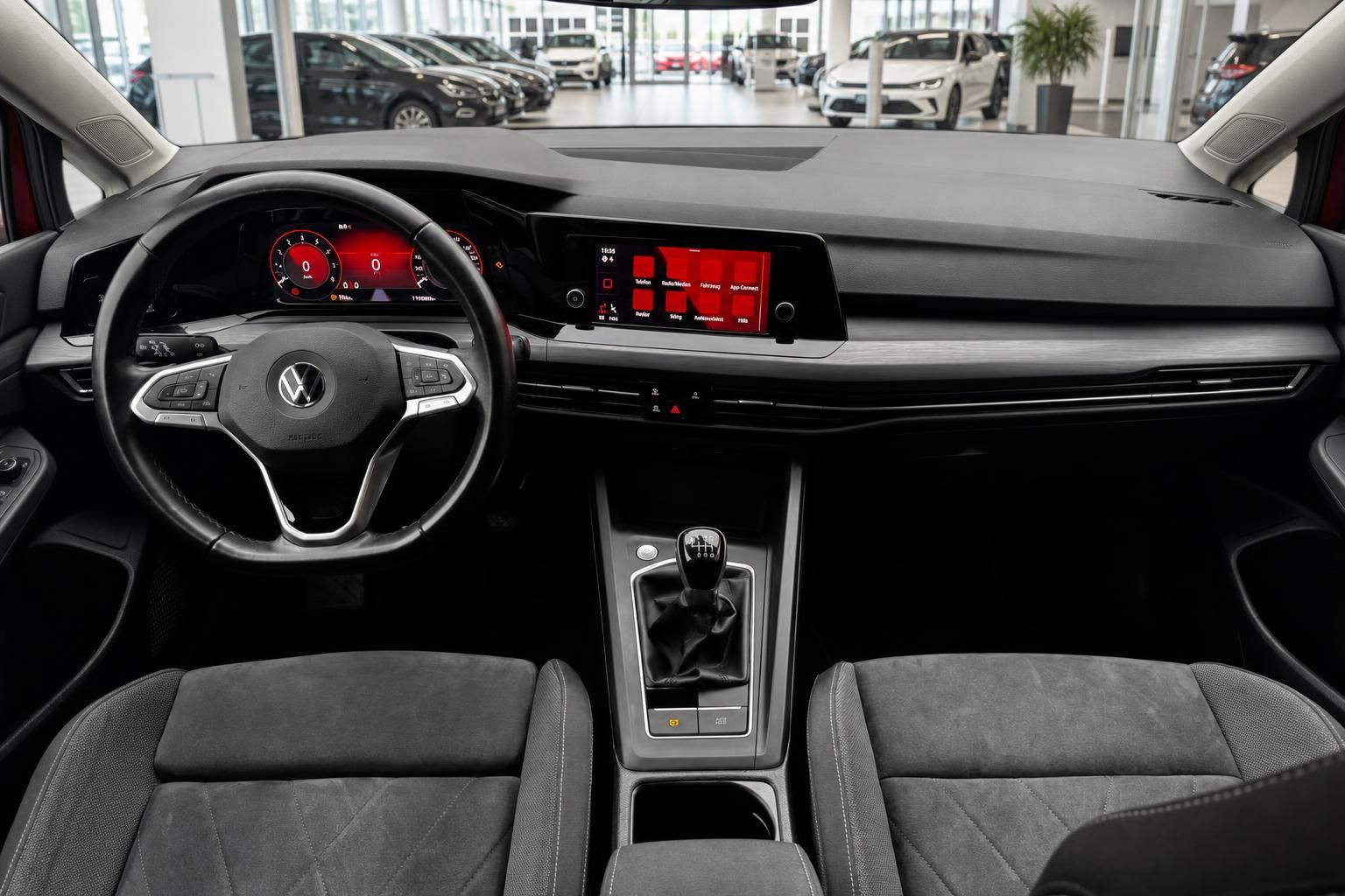 VW Golf Innenraum mit Lenkrad, Schaltgetriebe, Digitalcockpit und Infotainment-Display in rotem Design