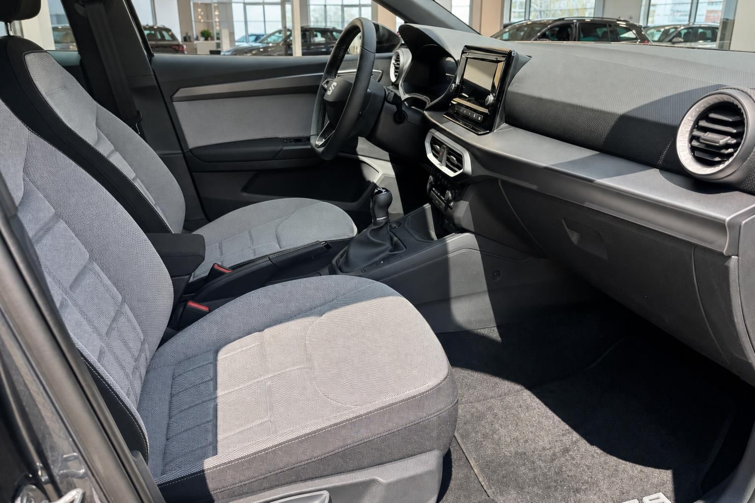 Fahrzeug Innenraum mit grauen Stoffsitzen, Schaltgetriebe, Lenkrad und Infotainment-Display