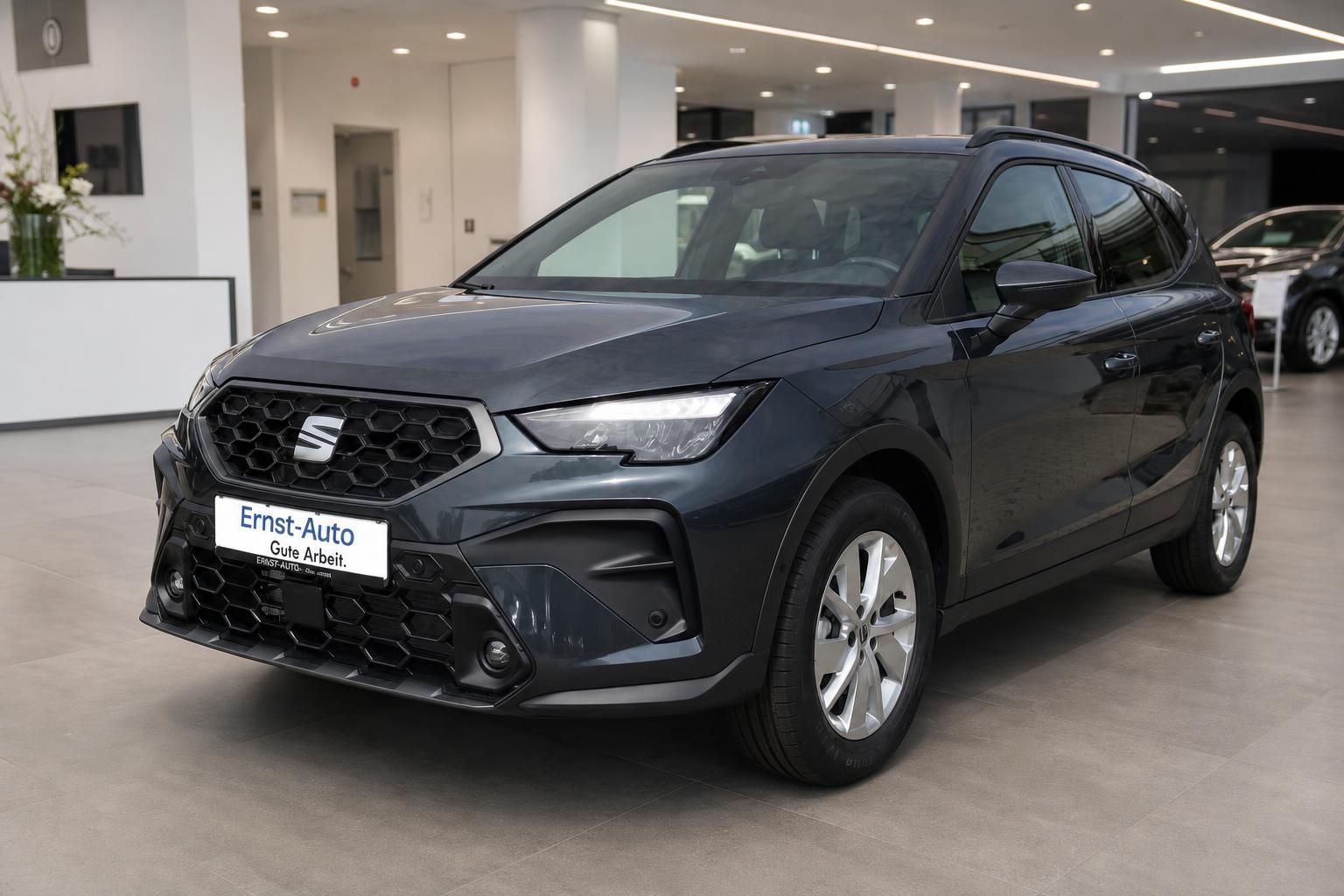 Grauer SEAT SUV Schrägansicht von vorne links auf Waldweg mit Bäumen im Hintergrund