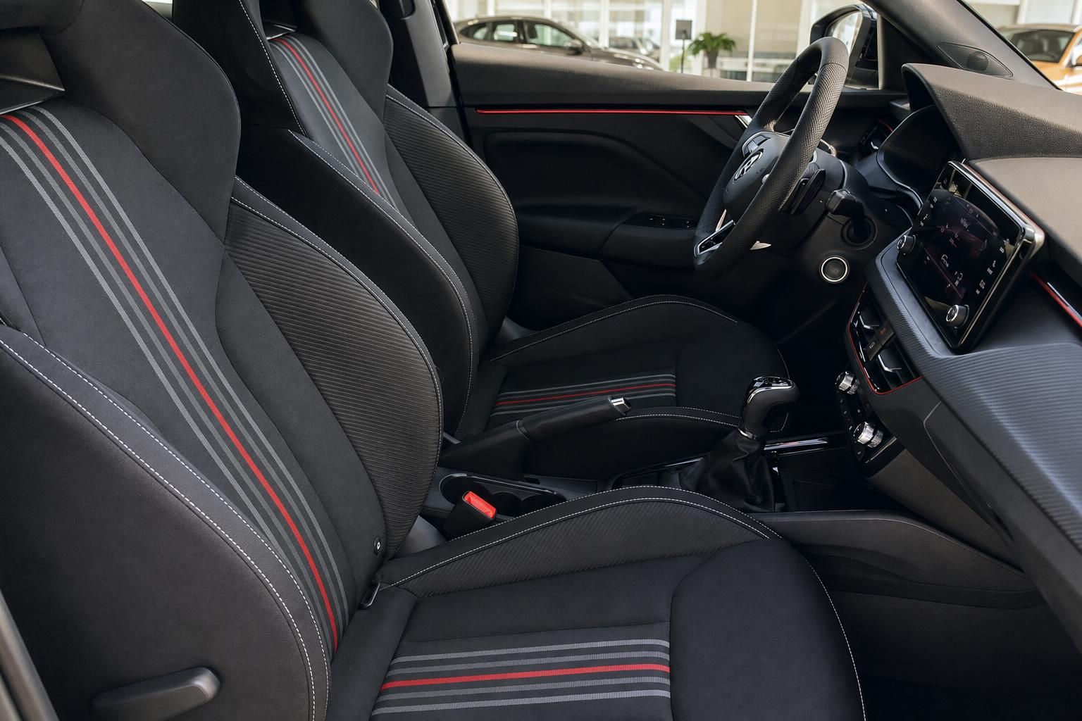 Fahrzeug Innenraum mit schwarzen Sportsitzen, roten Akzenten, Lenkrad und Touchscreen-Infotainment